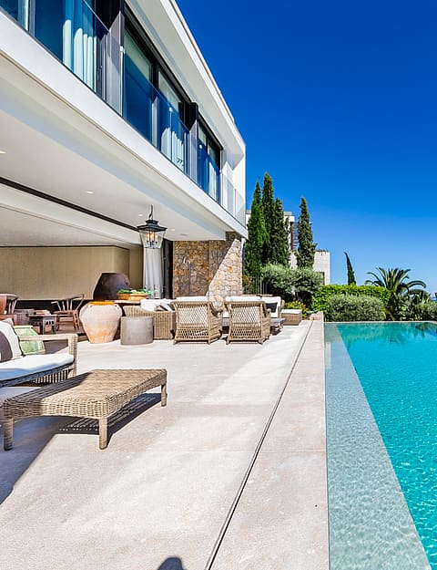 En infinity-pool med turkost vatten mot horisonten, intill en bred stenterrass med lounge-möbler.
