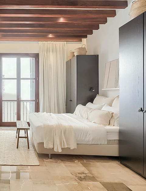 Spacious bedroom with exposed wood ceiling beams, stone flooring, a double bed, and glass doors leading to a balcony.
