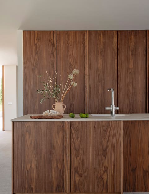 Close-up of a kitchen featuring vertical grain walnut cabinets, a light gray stone countertop, and a modern chrome faucet.