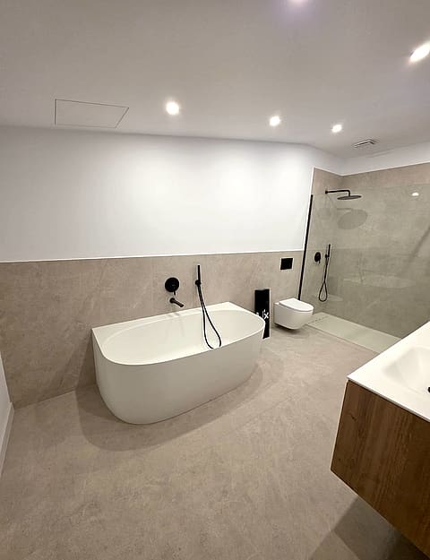 A modern bathroom featuring a white freestanding bathtub, beige stone floor tiles, a walk-in shower, and black fixtures.