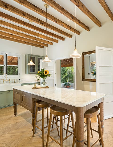 Traditional kitchen featuring sage green cabinetry, exposed timber ceiling beams, and a marble-topped central island.