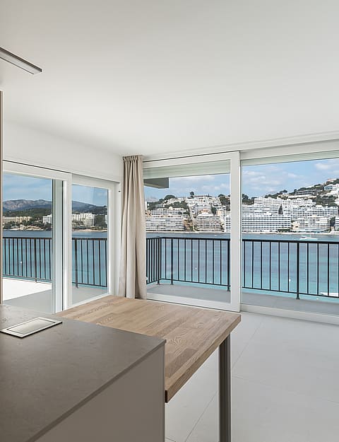 Modern taupe kitchen and wooden island extension facing floor-to-ceiling windows with a view of a coastal harbor.
