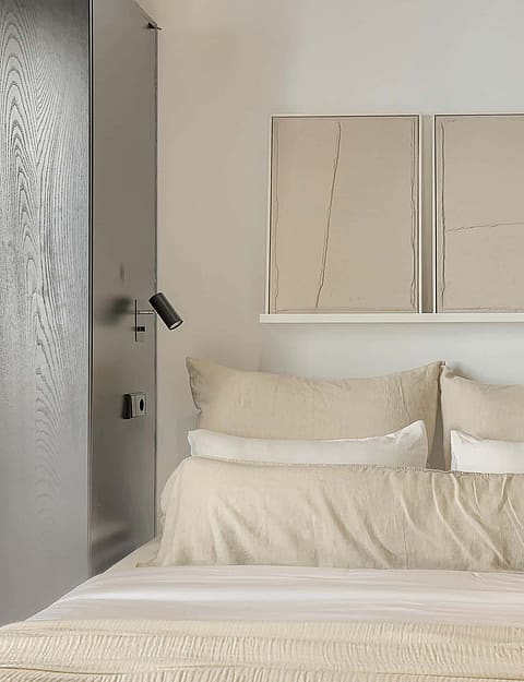 A symmetrical bedroom setup featuring a bed centered between two tall, grey, matte-finish cabinets with integrated wall lighting.
