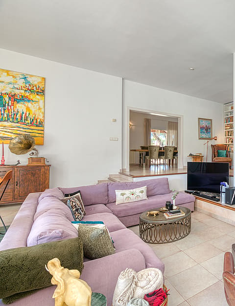 Spacious living room featuring a large lilac sectional sofa, a stone-fronted fireplace, and a light-colored tiled floor.