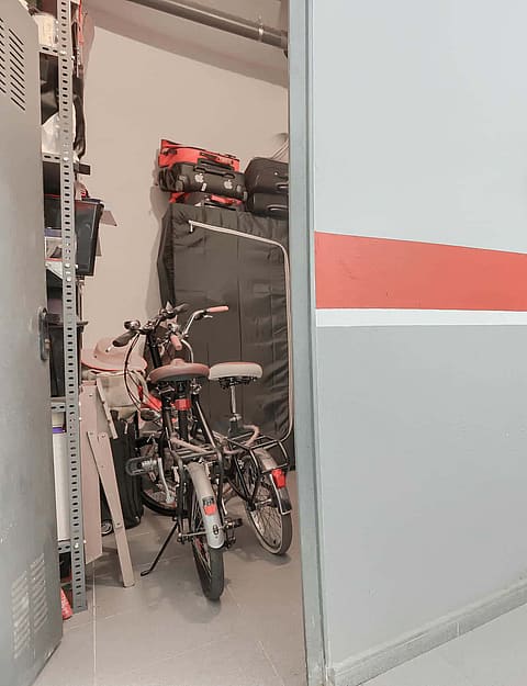 A private storage room with bicycles, located next to a grey painted wall with a fire extinguisher inside an underground parking garage.