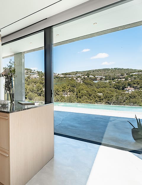 Contemporary kitchen featuring a light oak island, dark wood cabinetry, and large glass doors opening to a pool terrace.