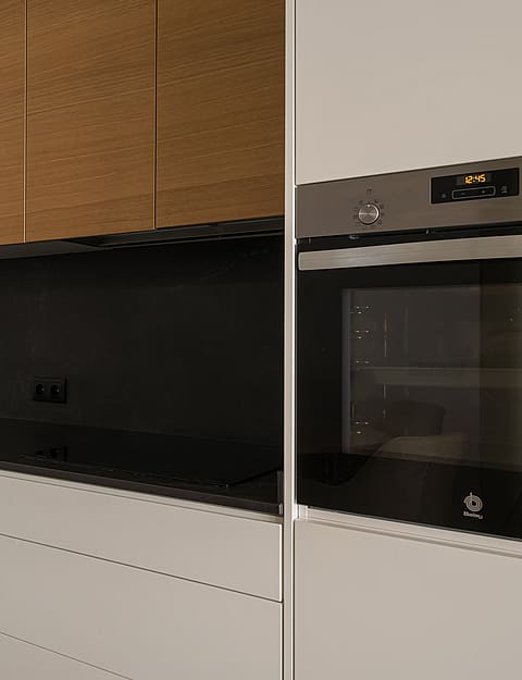 Modern kitchen featuring matte beige lower cabinets, wood veneer upper cabinets, and a black stone countertop.