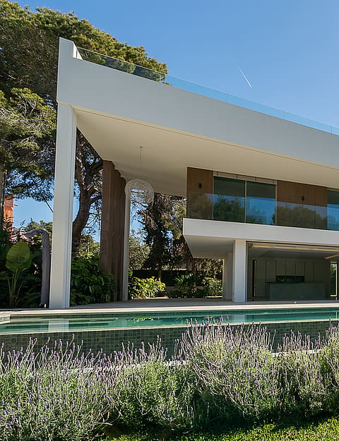 Exterior view of a two-story modern villa featuring a stone wall, glass railings, and a swimming pool in the foreground.