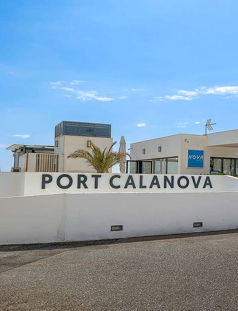Exterior view of the white facade and entrance signage for Port Calanova under a clear blue sky.