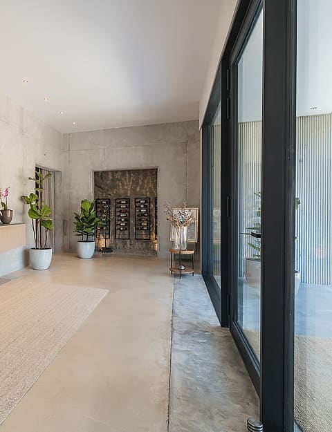 Minimalist hallway featuring raw concrete walls, floating oak storage, and a professional wine display at the far end.