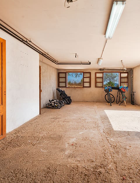 Garaje diáfano en finca rústica con suelo de grava, paredes blancas y gran apertura hacia el jardín.