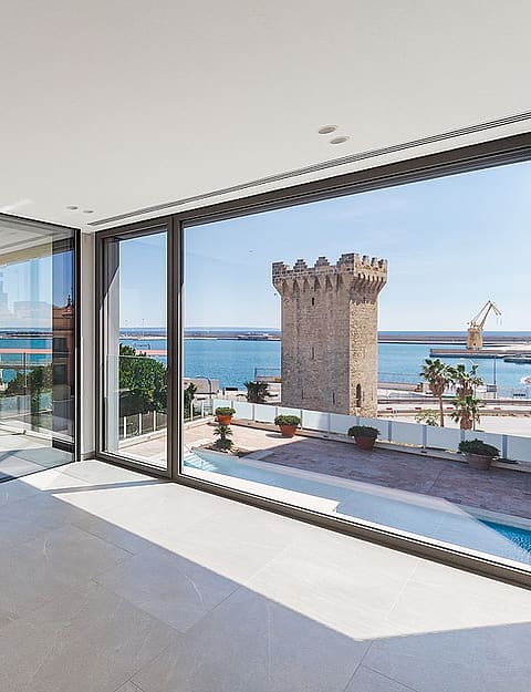 Light-filled corner living space with floor-to-ceiling glass on two elevations framing Palma harbour and open sea