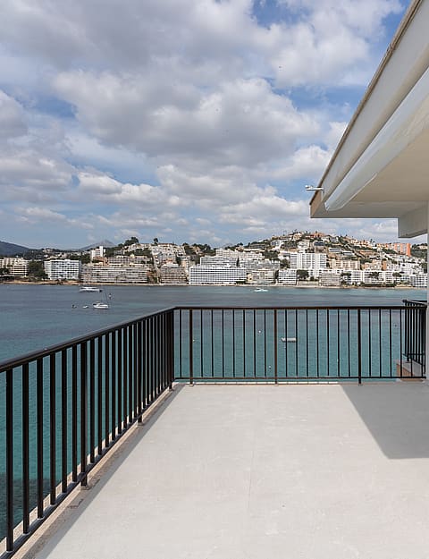 A spacious grey-tiled terrace with black metal railings faces a bay filled with boats under a cloudy sky.