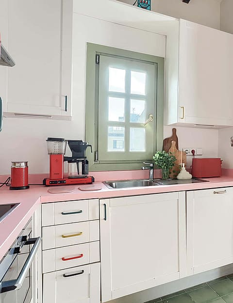 Kitchen featuring white cabinetry, a pink countertop, and a dining area with a round green table and wood chairs.