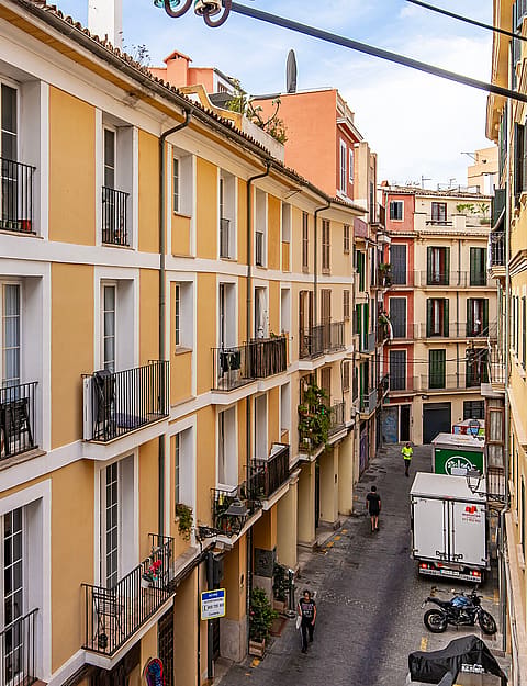 Exterior view of a traditional Mediterranean apartment building facade with mustard-yellow walls and green wooden shutters.