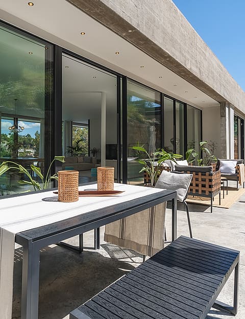 Contemporary stone terrace featuring a black metal dining set and floor-to-ceiling glass doors reflecting mountain views.