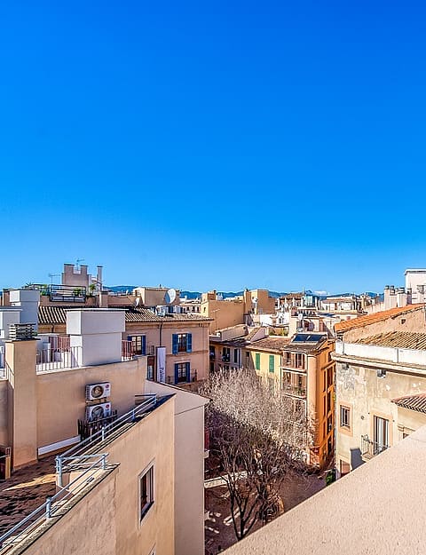 An elevated view from a rooftop terrace looking out over the densely packed stone buildings and terracotta roofs of an Old Town.