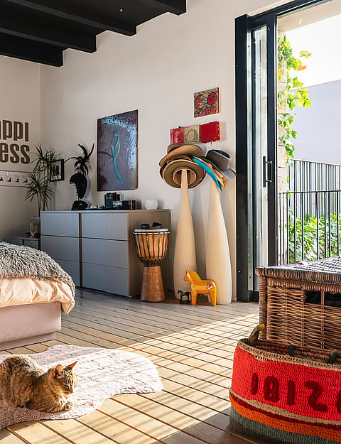 Interior of a bedroom featuring a platform bed, wooden floorboards, and glass doors opening to a garden, with eclectic decor.