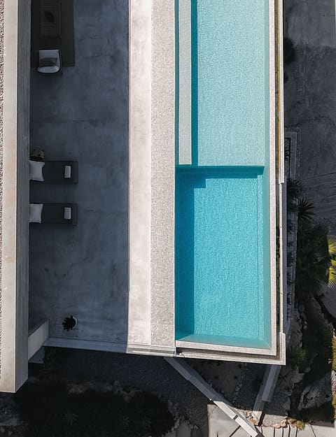 Top-down aerial shot of a rectangular turquoise pool, stone terrace with loungers, and a gravel-topped roof.