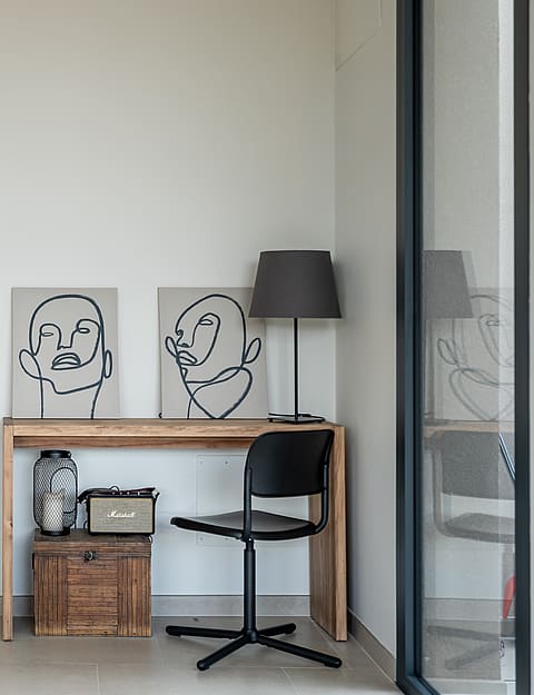 A minimalist hallway with a wooden desk and a black chair, featuring abstract line art prints against a white wall.