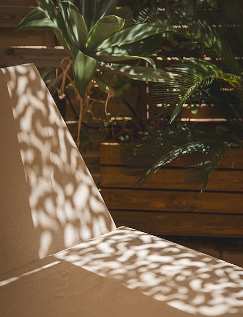 Close-up of a textured sun lounger on a terrace with wooden slats and tropical plants in the background.