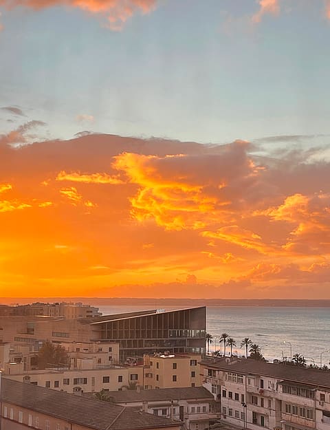 High-angle view overlooking old town rooftops and the sea during a vibrant orange and pink sunset.