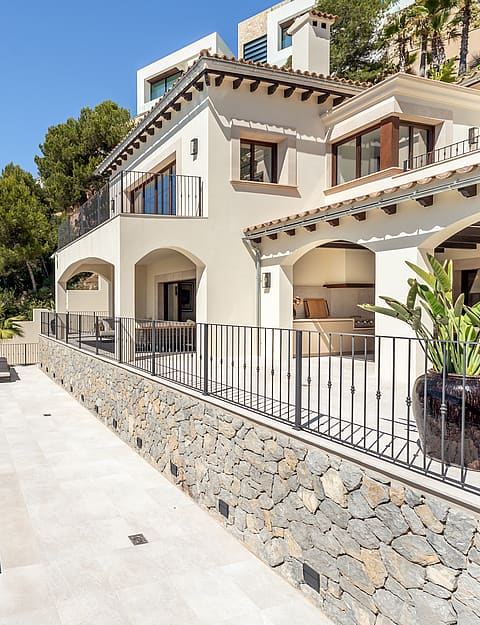 Exterior view of a cream stucco villa featuring arched terraces, wrought iron railings, stone walls, and a pool.