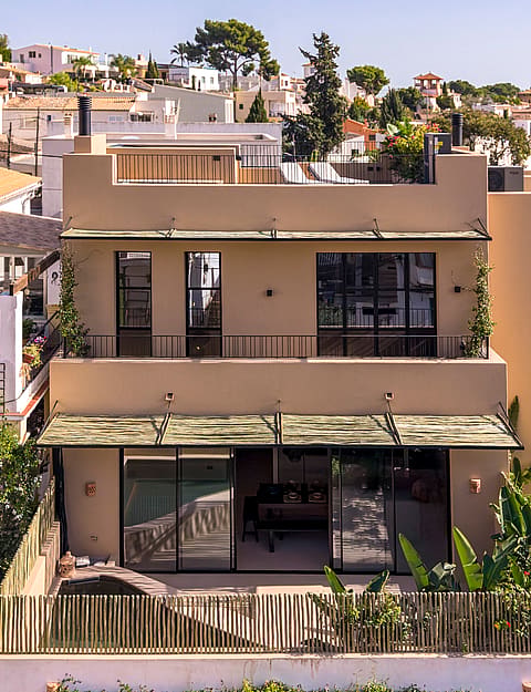 Front view of a two-story beige townhouse featuring modern black window frames, metal awnings, and glass sliding doors.