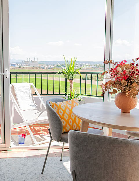 Dining room with a round wooden table, white chairs, and glass sliding doors opening to a balcony with mountain views.