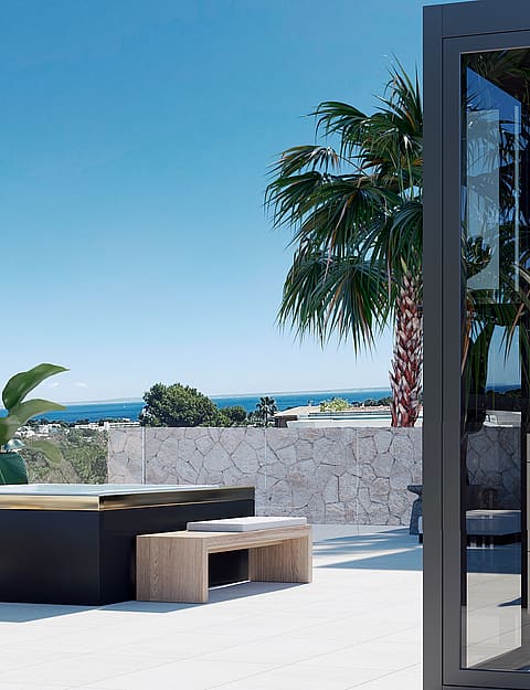 An elevated terrace with a dark-sided jacuzzi, light stone walls, and a view of the Mediterranean coastline.