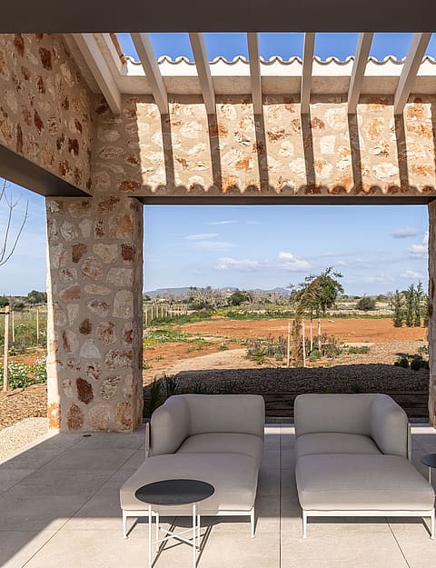 A stone-walled covered patio with modern outdoor seating, overlooking a rural landscape and distant mountains.