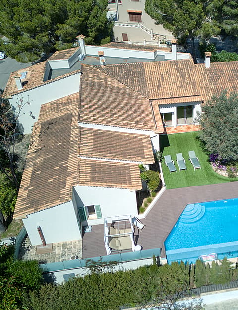 High-angle aerial shot of a residential villa featuring a terracotta tile roof, a swimming pool, and landscaped garden area.
