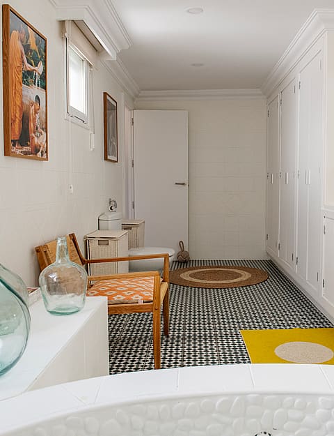 A bright bathroom with white walls, a patterned monochrome floor, and a large round basin in the foreground.