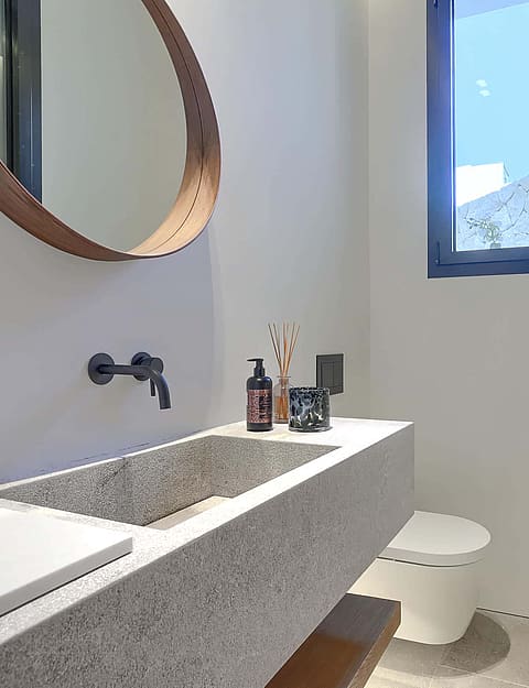 Modern bathroom featuring a textured stone floating vanity, circular wooden-framed mirror, and matte black wall-mounted faucet.