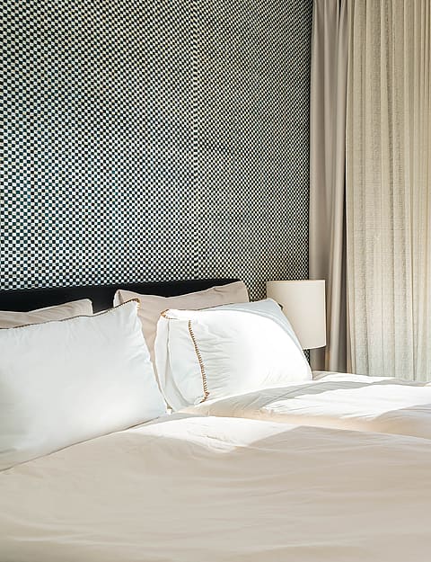 A bedroom corner featuring a black and white geometric patterned wallpaper, white bedding, and floor-to-ceiling glass doors.