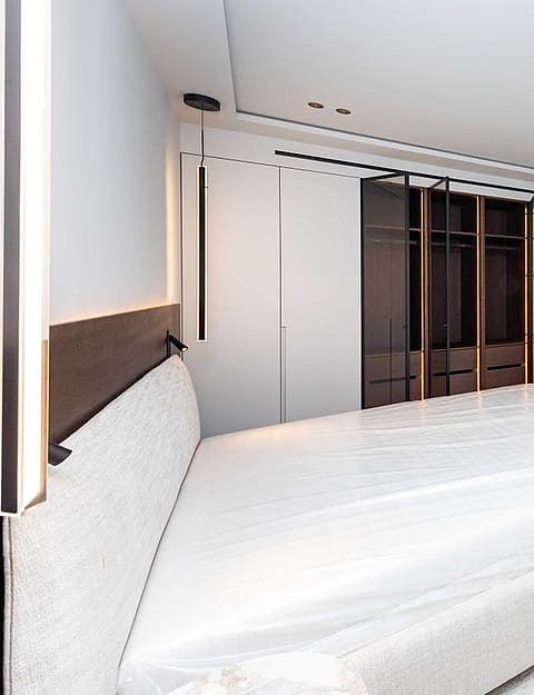 A modern bedroom featuring a large bed with an upholstered headboard, adjacent to a walk-in closet with dark glass doors.