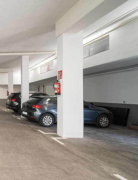 A clean, well-lit underground parking garage with concrete floors, white painted columns, and two parked cars.