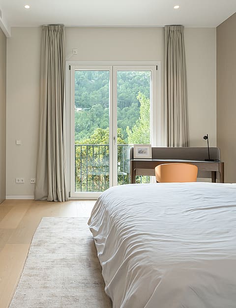 Bedroom with light wood floors, built-in wardrobes, a desk near the balcony door, and white bedding in a Son Vida villa.