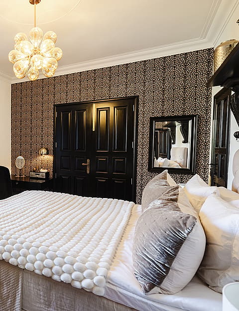 A bedroom with white walls, a black and white patterned feature wall, and tall black French doors opening to a garden.