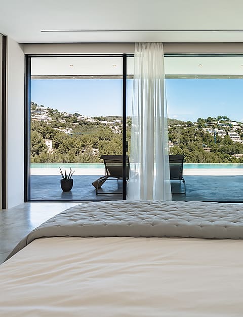 Contemporary master bedroom with large sliding glass doors facing a swimming pool and the Son Vida hills.