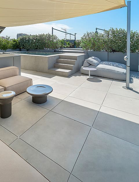 An expansive rooftop terrace with modular cream-colored seating, a glass balustrade, and a view overlooking the Mediterranean.