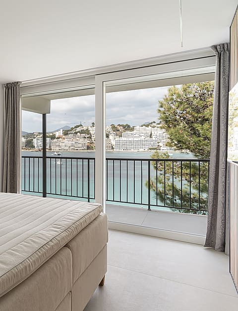 Modern master bedroom featuring a large sliding glass door opening to a private balcony with sea and town views.