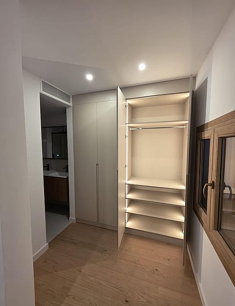 A modern dressing area featuring floor-to-ceiling built-in cabinetry with integrated LED lighting and light oak hardwood floors.