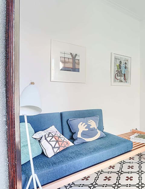 A small living space featuring a blue upholstered daybed, patterned floor tiles, a chrome side table, and a modern chair.