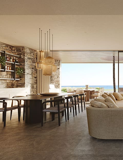 Wide-angle shot of a bright, open-plan living and dining room with floor-to-ceiling glass walls leading to an outdoor terrace, limestone fireplace, and Mediterranean sea views.