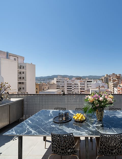 Outdoor dining table with marble top on a rooftop terrace overlooking Old Town buildings under a clear blue sky.