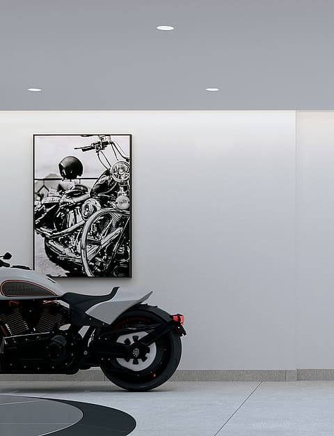 A modern, minimalist garage with white walls, recessed ceiling lights, and framed monochrome photography on the walls. A custom motorcycle is parked on a grey tiled floor.
