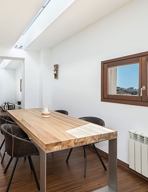 Modern dining area with oak table, dark chairs, and a long linear skylight over dark wood floors.