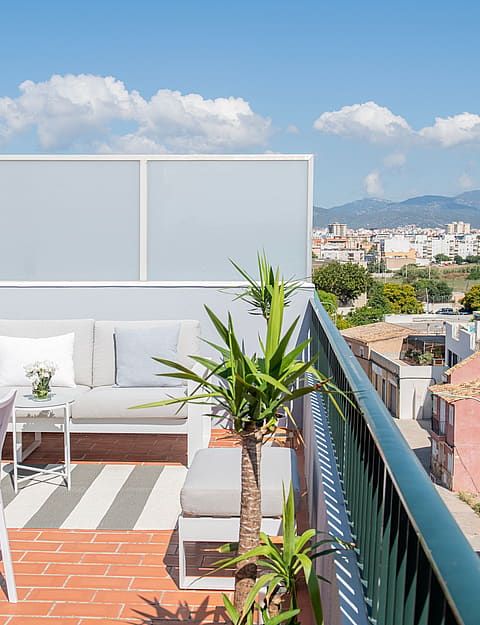 A sunny outdoor terrace in El Molinar featuring white seating, dining furniture, terracotta tiles, and views of distant mountains.