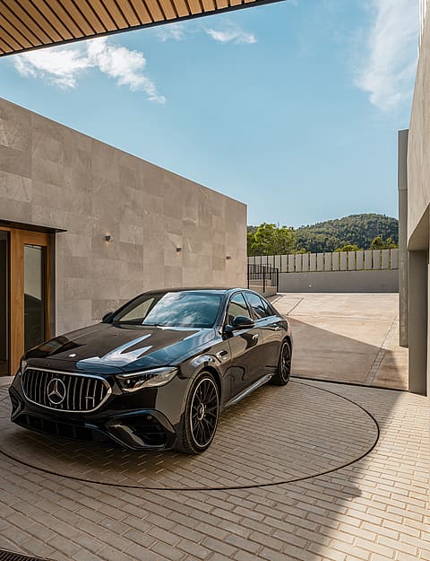 A black sedan parked on a circular metal turntable within a stone-walled courtyard under a bright blue sky.
